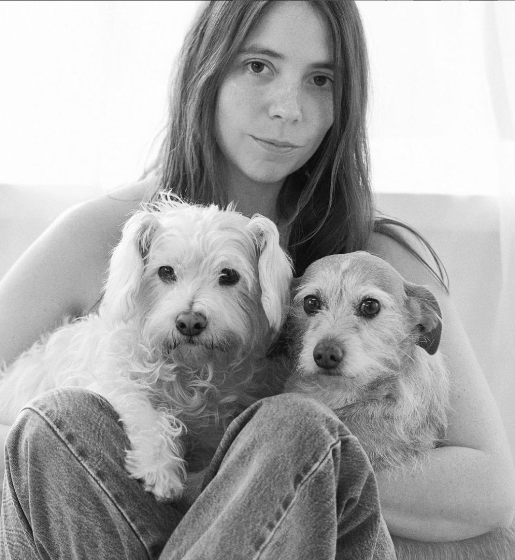 Elizabeth, founder of the clothing brand Foo and Foo, sitting with her two dogs, Hank and Finn. She has a calm expression as she holds both dogs close.