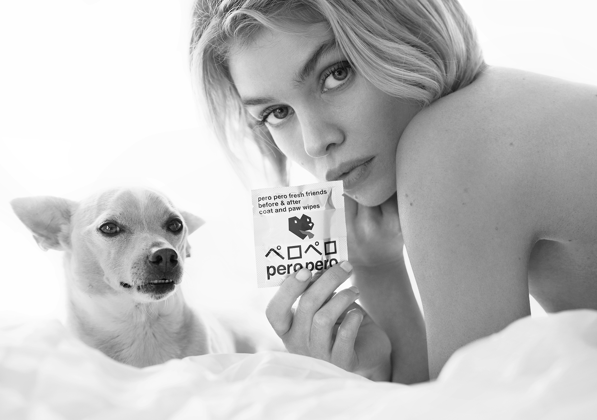 The image features Stella Maxwell, supermodel and founder of PeroPero, holding her Chihuahua-Terrier mix dog, Trip. Stella smiles warmly at the camera, dressed casually, with Trip cradled in her arms, looking relaxed. The PeroPero logo is present, reinforcing the brand's identity.